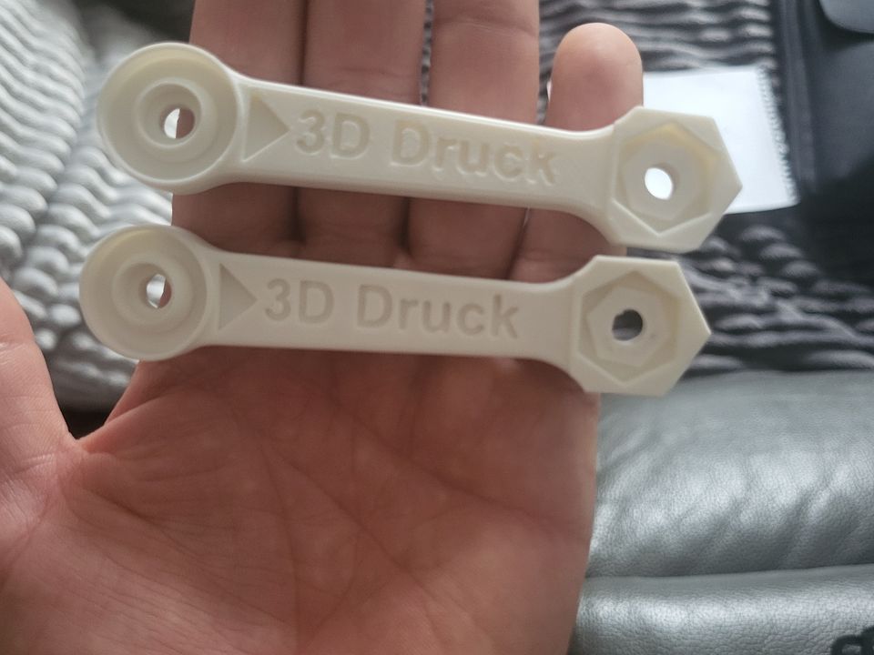 Zwei weiße Kleinteile mit der Prägung 3D Druck auf einer Handfläche